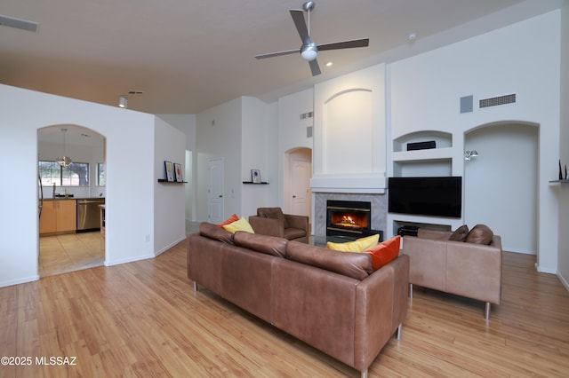 living room with visible vents, arched walkways, light wood finished floors, a premium fireplace, and ceiling fan