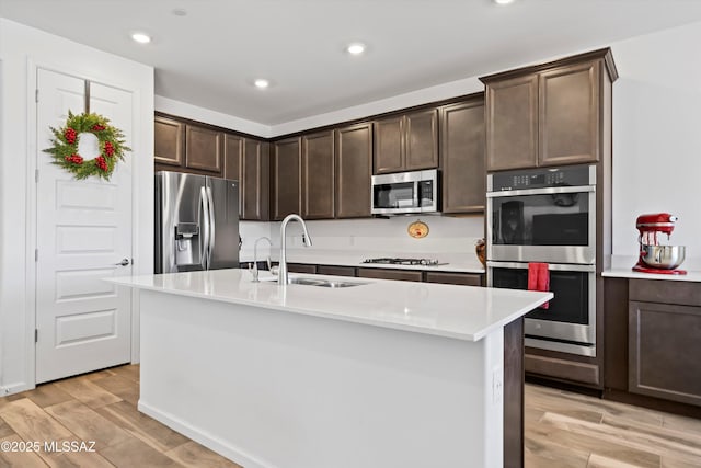 kitchen with stainless steel appliances, light countertops, a sink, and an island with sink