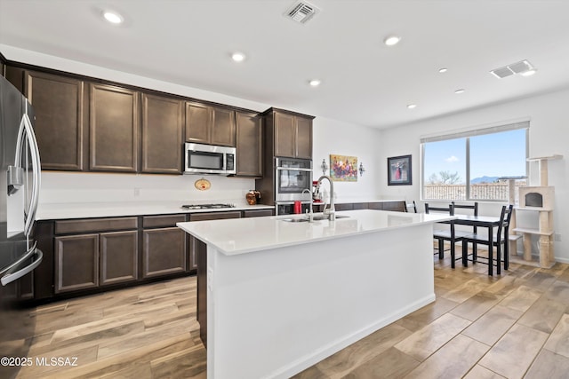 kitchen with a center island with sink, visible vents, stainless steel appliances, light countertops, and light wood-type flooring
