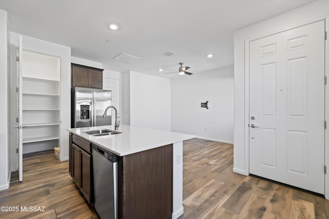 kitchen featuring light countertops, appliances with stainless steel finishes, a sink, an island with sink, and dark brown cabinets