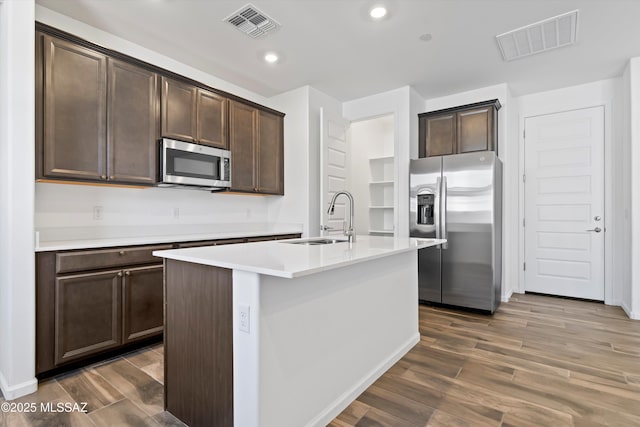 kitchen featuring stainless steel appliances, light countertops, visible vents, a sink, and an island with sink