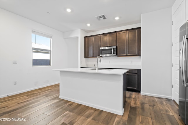 kitchen featuring light countertops, stainless steel microwave, a center island with sink, and visible vents