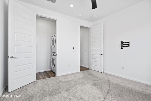 unfurnished bedroom with stacked washer and dryer, dark colored carpet, visible vents, and baseboards