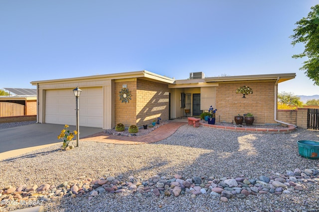 mid-century modern home featuring a garage, central AC unit, concrete driveway, fence, and brick siding