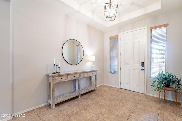 foyer featuring an inviting chandelier, a tray ceiling, light tile patterned flooring, and baseboards