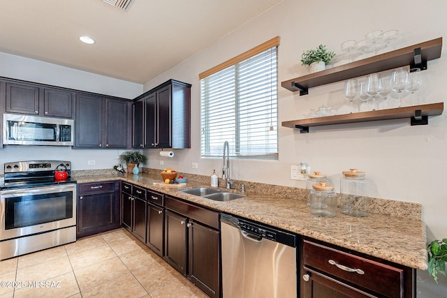 kitchen with light tile patterned floors, appliances with stainless steel finishes, light stone countertops, and a sink