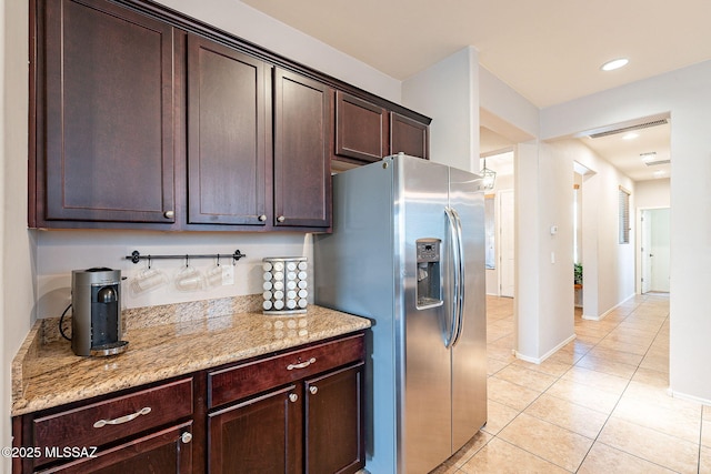 kitchen with stainless steel refrigerator with ice dispenser, recessed lighting, light tile patterned flooring, light stone countertops, and dark brown cabinets