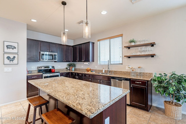 kitchen featuring a sink, a kitchen island, appliances with stainless steel finishes, light tile patterned flooring, and light stone countertops