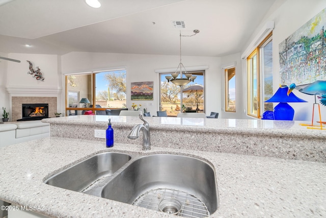 kitchen with lofted ceiling, sink, decorative light fixtures, a tile fireplace, and light stone countertops