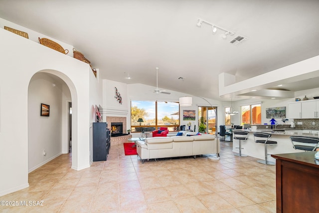 tiled living room with ceiling fan, track lighting, and vaulted ceiling