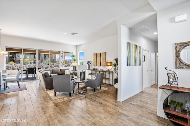 living area with attic access, visible vents, light wood finished floors, and a chandelier