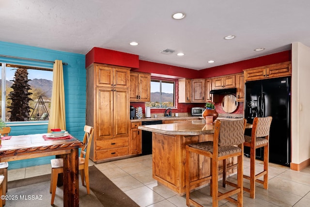 kitchen featuring sink, light tile patterned floors, light stone counters, black appliances, and a kitchen island