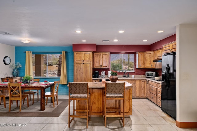 kitchen with light tile patterned flooring, a kitchen island, a breakfast bar, sink, and black fridge