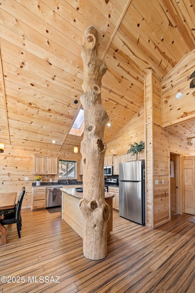 kitchen featuring a skylight, stainless steel appliances, wood ceiling, light brown cabinets, and wooden walls