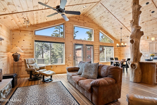 living area with hardwood / wood-style flooring, wood ceiling, wood walls, high vaulted ceiling, and ceiling fan with notable chandelier