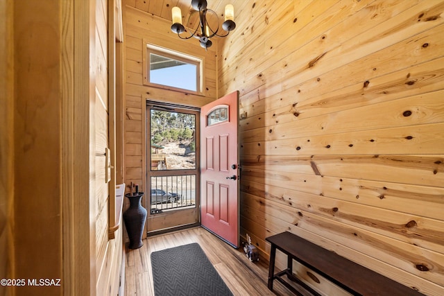 doorway to outside with a notable chandelier, light wood-type flooring, and wooden walls