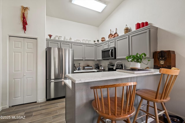 kitchen featuring a peninsula, appliances with stainless steel finishes, a breakfast bar area, and gray cabinets