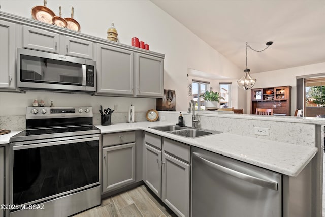 kitchen featuring appliances with stainless steel finishes, a peninsula, vaulted ceiling, gray cabinets, and a sink