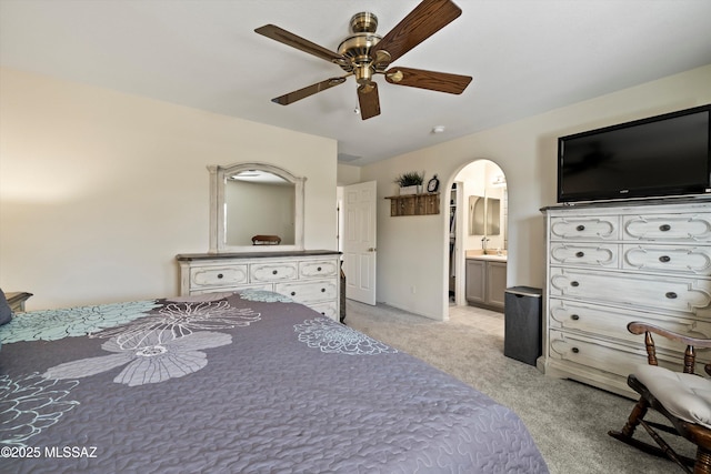 unfurnished bedroom featuring a ceiling fan, arched walkways, light carpet, and connected bathroom