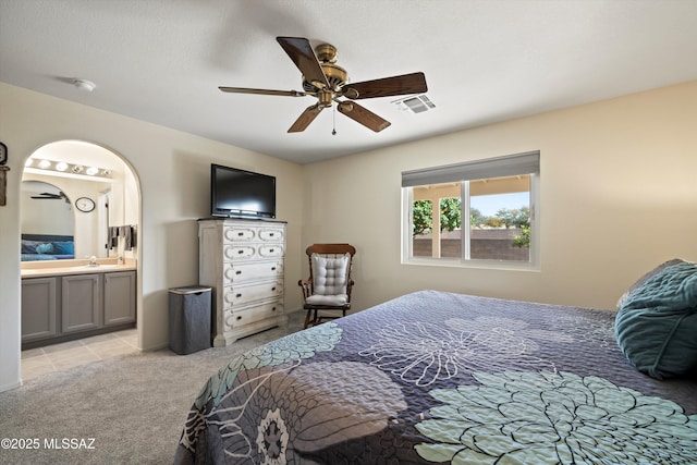 bedroom with a ceiling fan, light colored carpet, visible vents, and ensuite bath