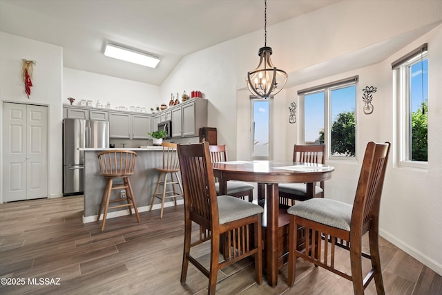 dining space with a chandelier, lofted ceiling, light wood-style flooring, and baseboards