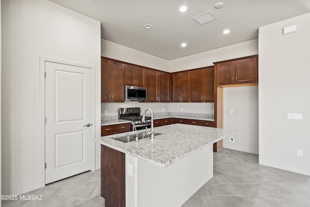 kitchen featuring light stone counters, visible vents, a kitchen island with sink, a sink, and appliances with stainless steel finishes