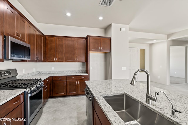 kitchen featuring light stone countertops, visible vents, appliances with stainless steel finishes, and a sink