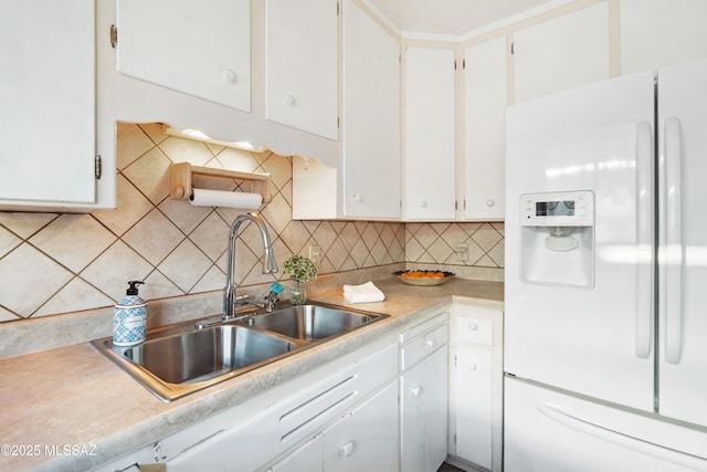 kitchen with a sink, white cabinetry, light countertops, backsplash, and white fridge with ice dispenser