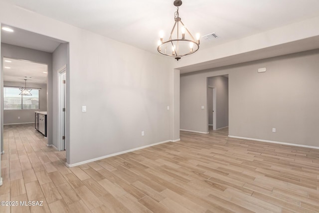 empty room featuring a notable chandelier and light hardwood / wood-style floors