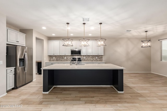 kitchen featuring hanging light fixtures, appliances with stainless steel finishes, a kitchen island with sink, decorative backsplash, and white cabinets