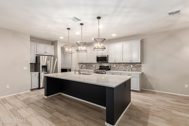 kitchen with sink, decorative light fixtures, an island with sink, stainless steel appliances, and white cabinets