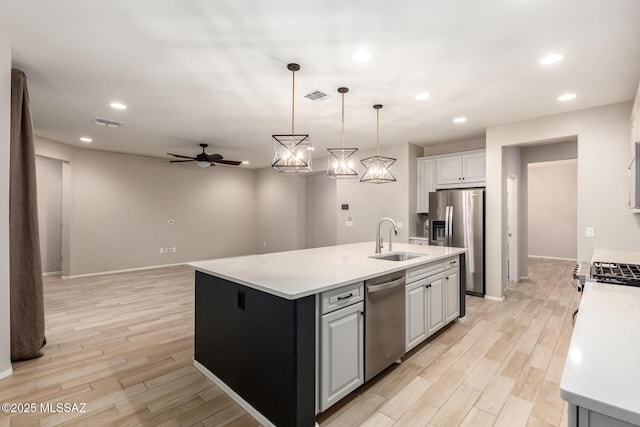 kitchen with decorative light fixtures, sink, light hardwood / wood-style floors, stainless steel appliances, and a center island with sink