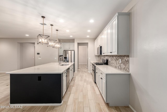 kitchen featuring sink, hanging light fixtures, appliances with stainless steel finishes, a kitchen island with sink, and backsplash