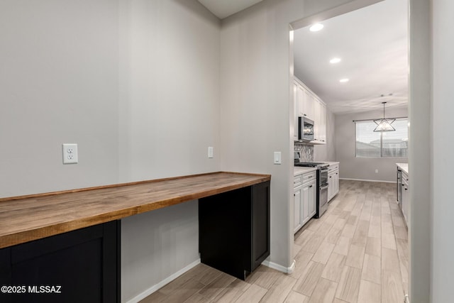 kitchen with appliances with stainless steel finishes, butcher block countertops, hanging light fixtures, and white cabinets