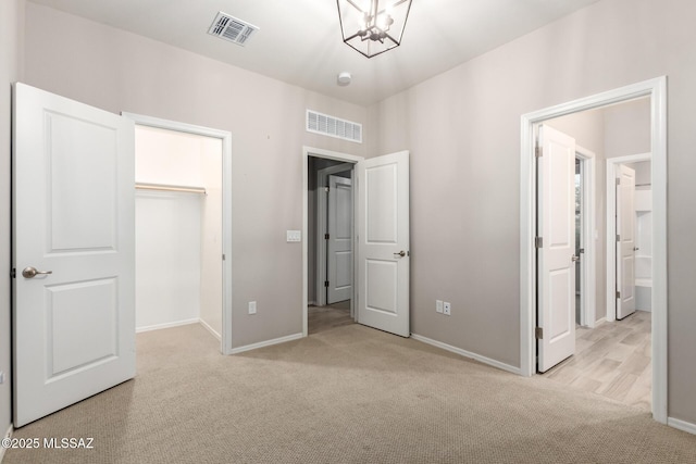 unfurnished bedroom with a walk in closet, light colored carpet, a chandelier, and a closet