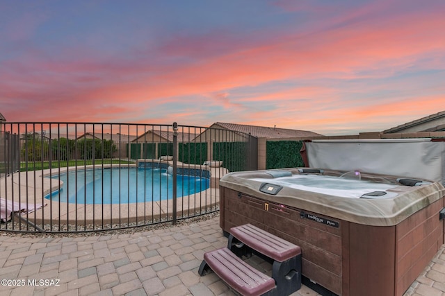 pool at dusk with a hot tub and a patio