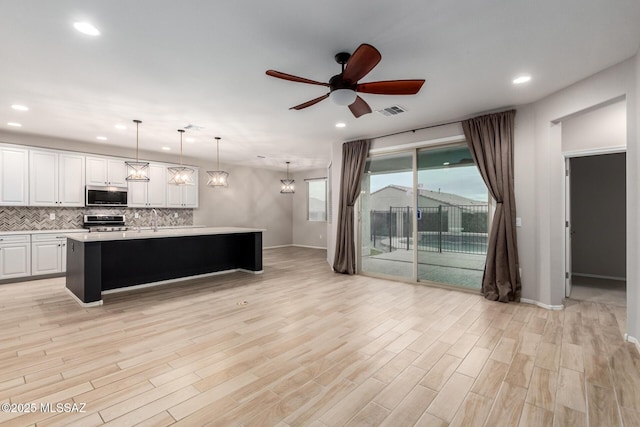 kitchen with pendant lighting, tasteful backsplash, white cabinets, stainless steel appliances, and a center island with sink