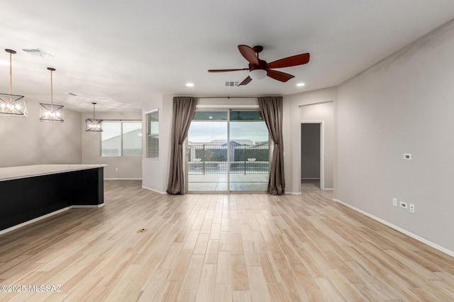 spare room featuring ceiling fan with notable chandelier and light wood-type flooring