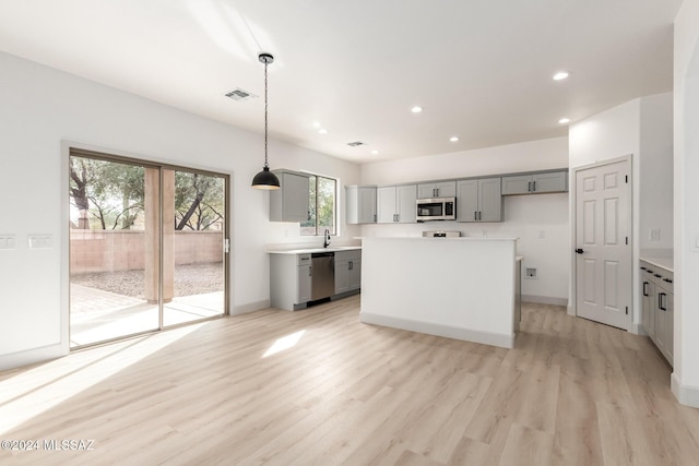 kitchen featuring gray cabinetry, a center island, pendant lighting, stainless steel appliances, and light hardwood / wood-style floors