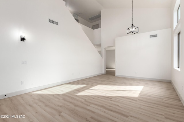 unfurnished room with an inviting chandelier, high vaulted ceiling, and light hardwood / wood-style flooring