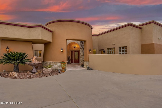 entrance to property featuring stone siding, a patio area, fence, and stucco siding