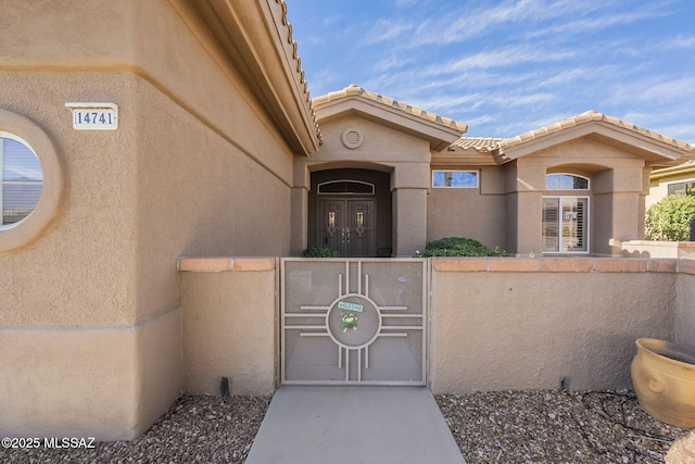 view of exterior entry featuring a tile roof, fence, a gate, and stucco siding