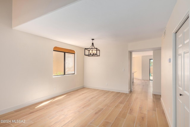 unfurnished room featuring an inviting chandelier, light hardwood / wood-style flooring, and a wealth of natural light