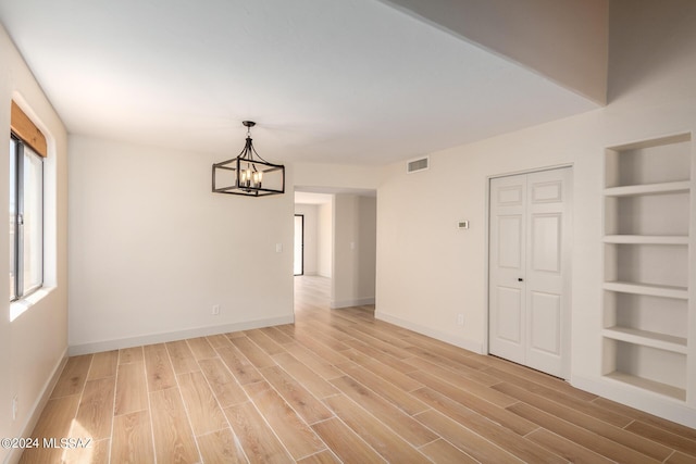 unfurnished room with an inviting chandelier, light hardwood / wood-style floors, and built in shelves