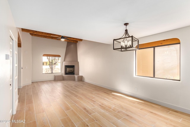 unfurnished living room featuring beamed ceiling, a large fireplace, ceiling fan with notable chandelier, and light hardwood / wood-style flooring