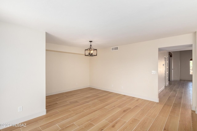 unfurnished room with an inviting chandelier and light hardwood / wood-style flooring