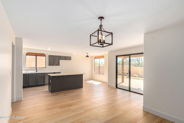 kitchen with a kitchen island, pendant lighting, sink, a notable chandelier, and light hardwood / wood-style floors