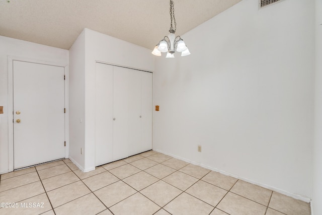 unfurnished dining area with light tile patterned floors, a textured ceiling, and a chandelier