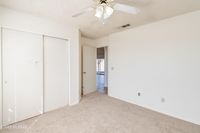 unfurnished bedroom featuring ceiling fan, light carpet, a textured ceiling, and a closet