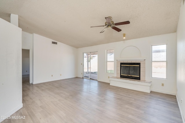 unfurnished living room with lofted ceiling, a textured ceiling, a tile fireplace, ceiling fan, and light hardwood / wood-style floors